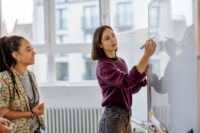 Businesswoman brainstorming ideas on whiteboard with colleague