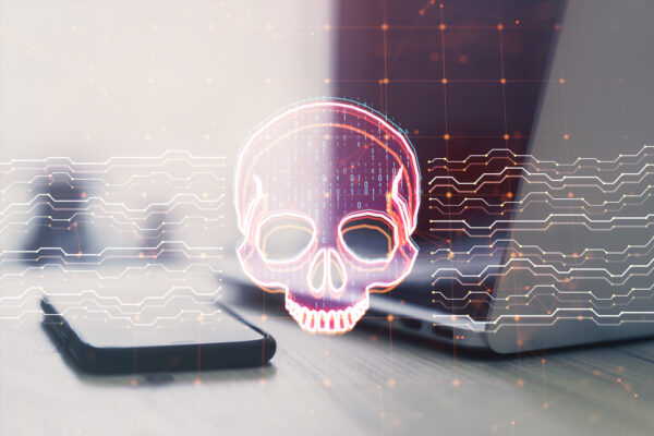 Close up of laptop and smartphone on desk with creative skull and circuit hologram on blurry background Malware and ransomware concept Double exposure